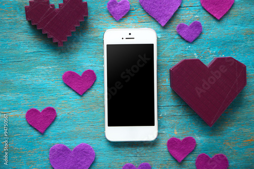 Smart phone with blank screen and hearts on old wooden table