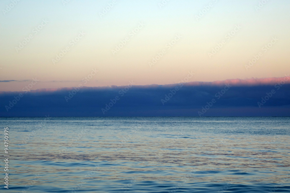 Fototapeta premium Calm ocean waters of Waimanalo Bay at dusk with clouds hanging o