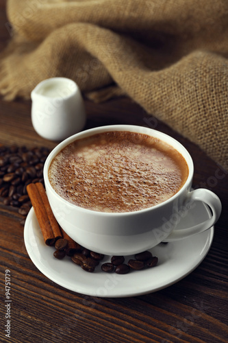 Cup of coffee with cream and coffee beans on wooden background