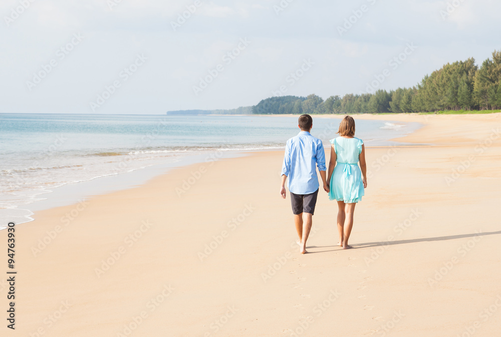 Back view of loving couple walking away on sandy beach