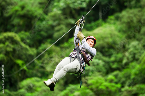 A group of people in climbing gear zip lining through the forest canopy on a wire suspended high above the jungle floor. photo
