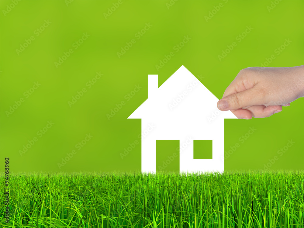 Conceptual white paper house symbol held in hand in green grass Conceptual white paper house symbol held in hand in green grass