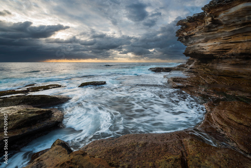 Seascape sunrise with unrest sea and grim sky and cliffs