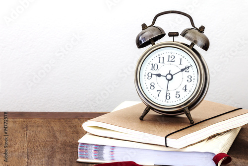 a vintage alarm clock and books on wooden table with copy space