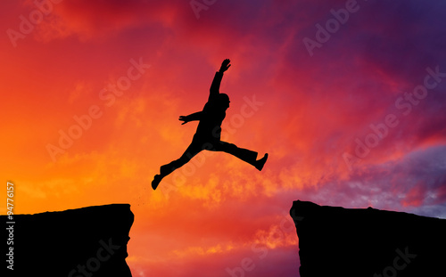 Man jumping across the gap from one rock to cling to the other.