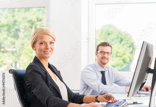 Beautiful female office worker in formalwear with colleague on background.