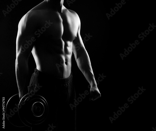 Strong, fit and sporty bodybuilder man with a dumbbell in monoch