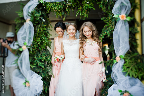 smiled bride with bridesmaids under decor pine arch photo