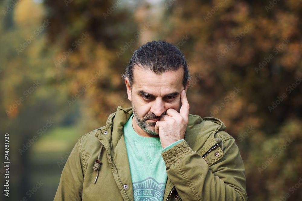 Worried man outside in a park, hand covering face, fall season Worried man outside in a park, hand covering face, fall season