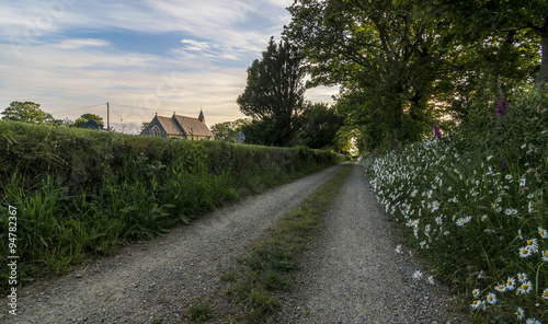 A deserted country path, with wild flowers growing in the verge and a quaint church on the horizon