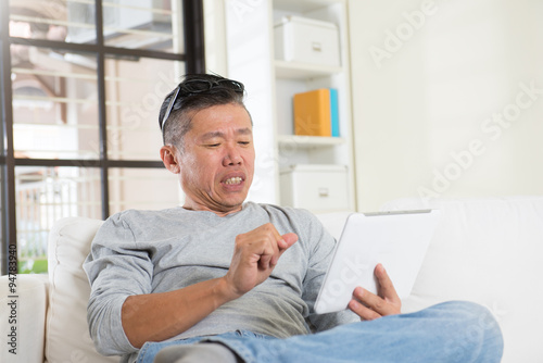 unhappy asian senior using tablet