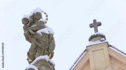 Statue of Virgin Mary and Jesus in the background church in the winter and snowing
