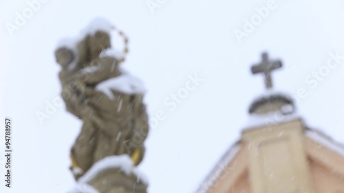 Statue of Virgin Mary and Jesus in the background church in the winter and snowing