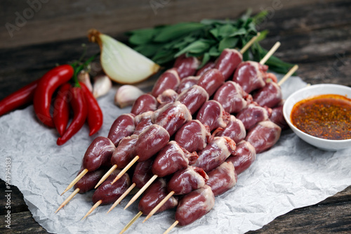 Ready to cook Duck Heart stringed on skewers BBQ with hot sauce and chili pepper. decorated with greens and vegetables. background