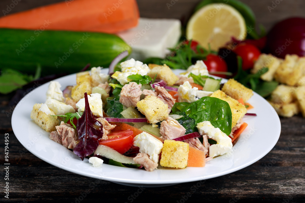 Tuna salad with Spinach, rocket, red ruby chard, tomatoes, cucumbers, carrot, red onion, white chesse, croutons on old wooden table