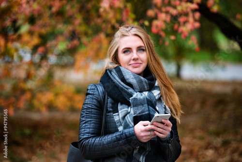 Beautiful happy woman walking and texting in the autumn park