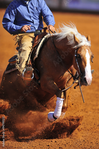 A close up view of a rider sliding the horse in the dirt