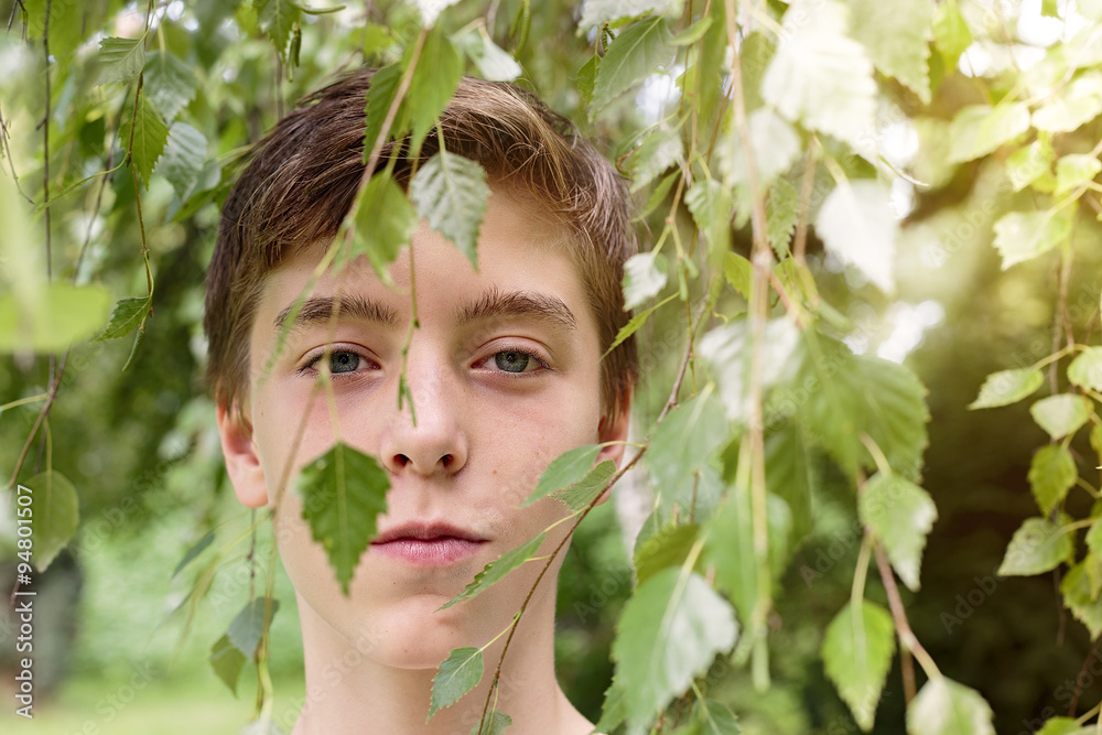 portrait of a teenage boy hidden by some leaves