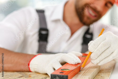 Attractive male carpenter is taking measurements of material
