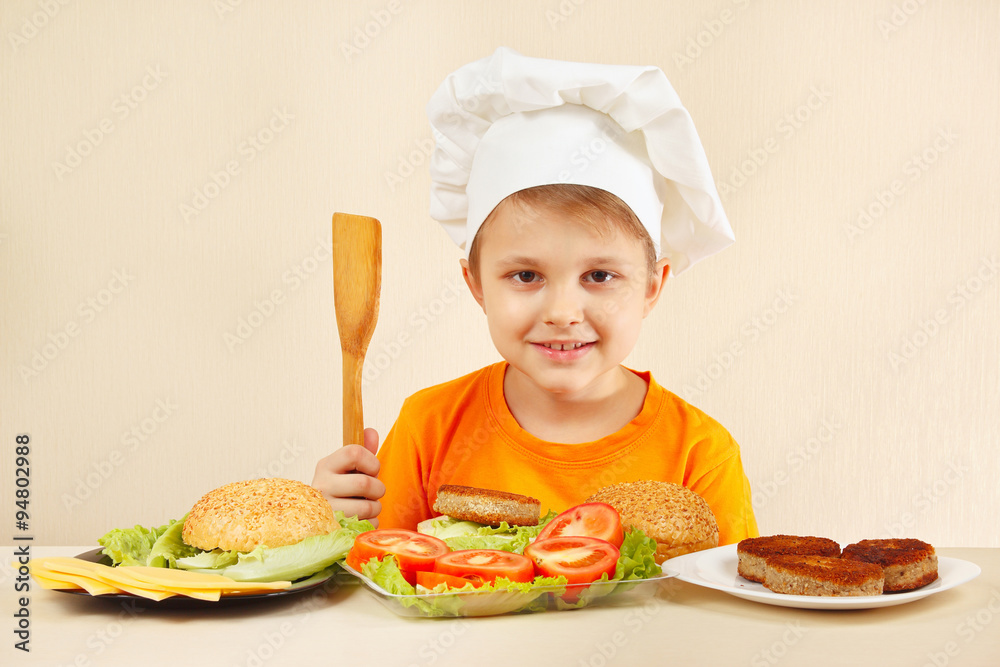 Young smiling chef at the table with ingredients is going to cook a hamburger Young smiling chef at the table with ingredients is going to cook a hamburger