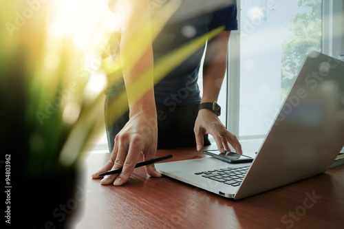 designer hand working laptop with green plant foreground on wood