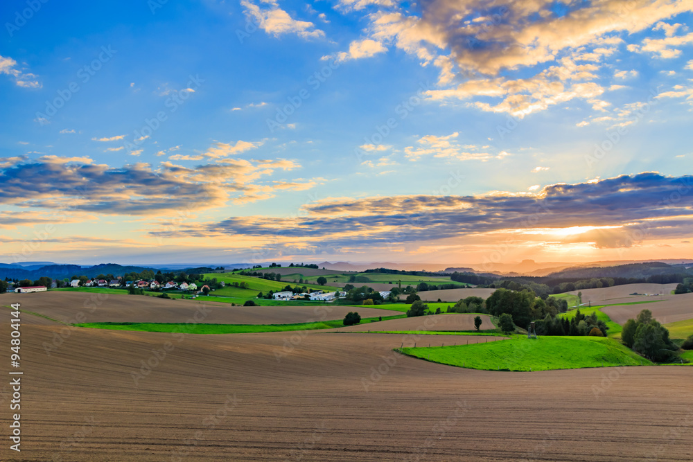 Fototapeta premium Beautiful sunset over countryside landscape of rolling hills with sun beams piercing sky and lighting hillside