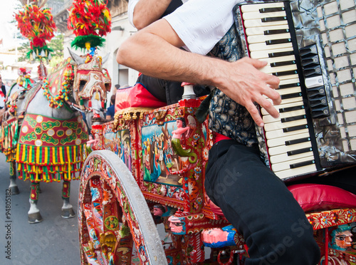 Accordion player wearing a folkloristic dress and playing on a characteristic sicilian cart