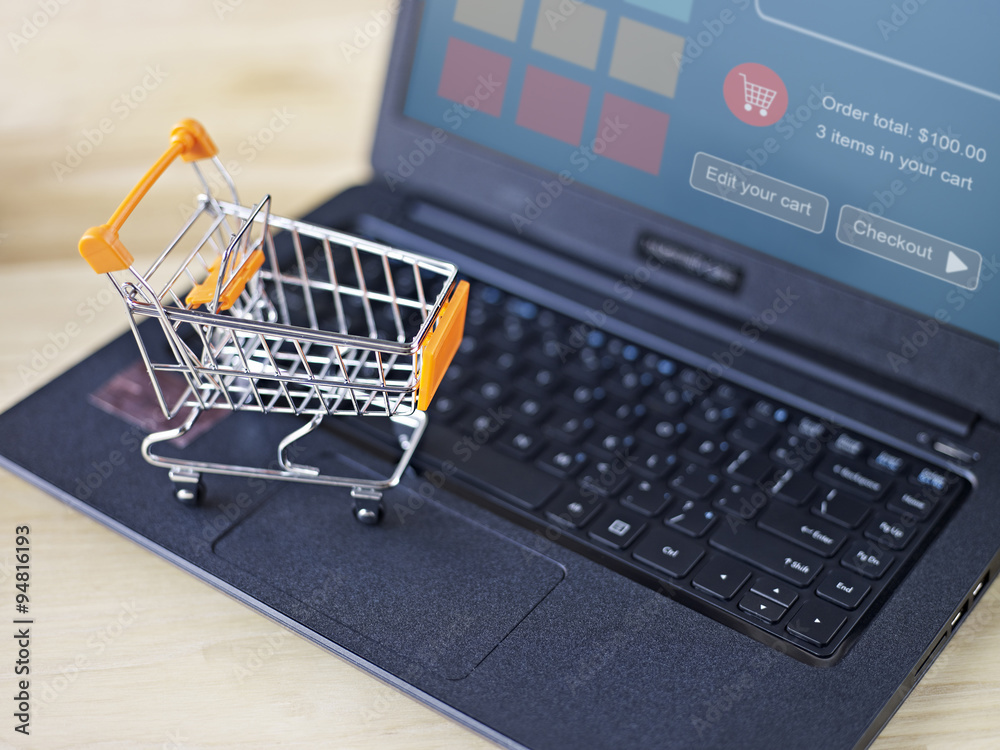 toy shopping cart on laptop; home shopping and e-commerce concept