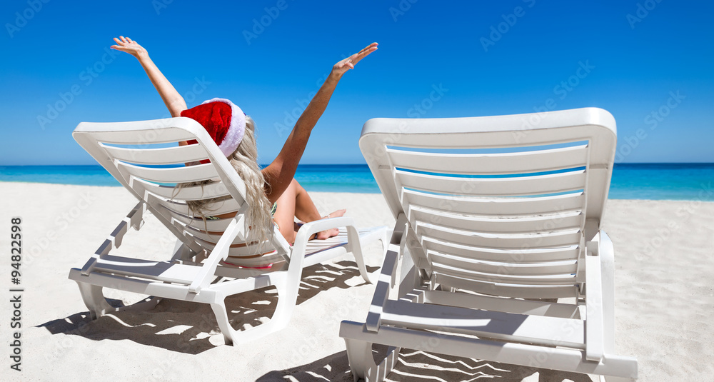 Obraz premium Happy woman in Santa Helper Hat sitting on sunbed with outstretc