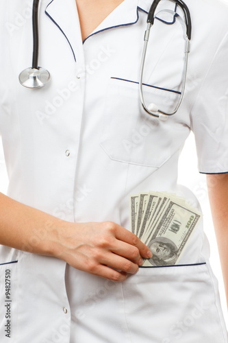 Woman doctor with stethoscope and currencies dollar in apron pocket, corruption or bribe concept