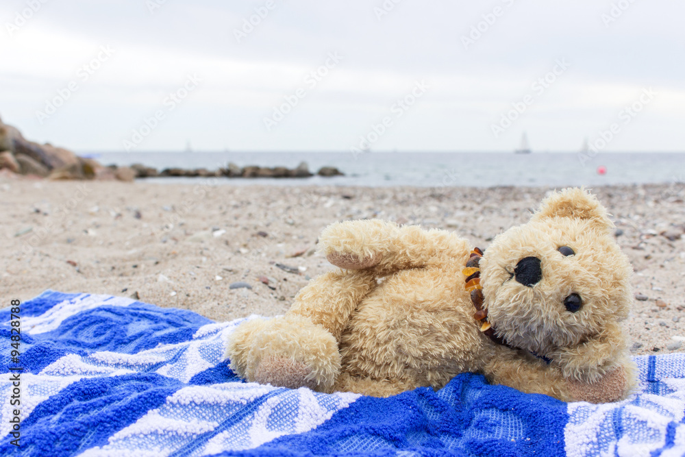 teddy bear A teddy bear lies on a beach towel on the Baltic beach Stock Adobe Stock