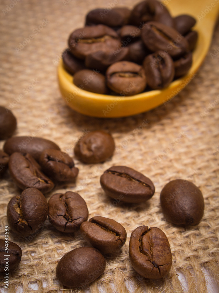 Naklejka premium Heap of coffee beans with wooden spoon on jute canvas