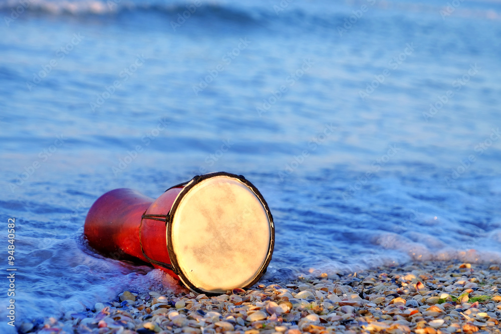 Beautiful ethnic drum with seashells on the beach on sunrise background Beautiful ethnic drum with seashells on the beach on sunrise background