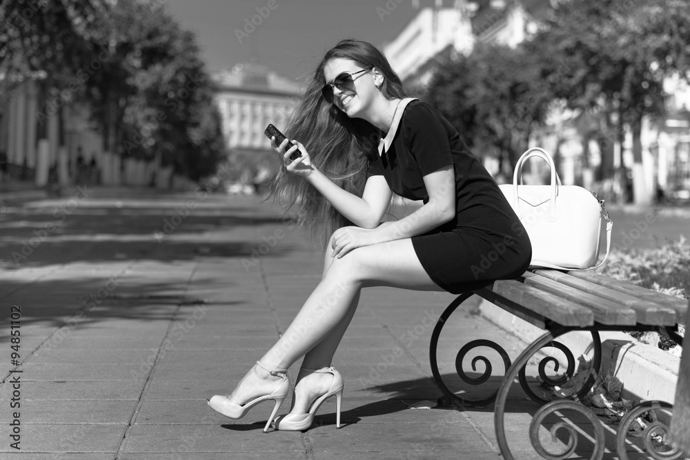Fototapeta premium young businesswoman with phone sitting on the bench
