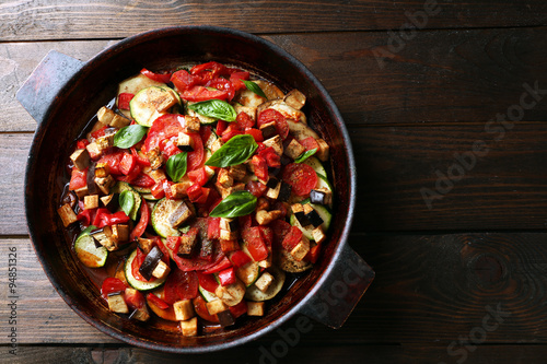 Tasty vegetarian ratatouille made of eggplants, squash, tomatoes and onions in black cast iron pan, on wooden table background