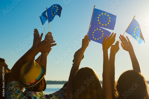 People with raised hands waving flags of the European Union. 