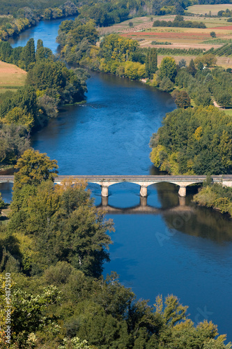 View over the Dordogne river seen from Domme village. The bridge over the river in Domme city. Medieval bridge crossing blue river in Perigord region. Bastide town in Dordogne, France.