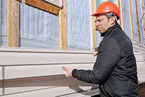 A worker installs panels beige siding on the facade