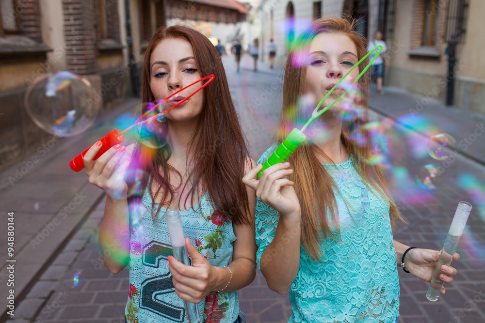Two pretty girls having fun and blowing bubbles. Urban background.
