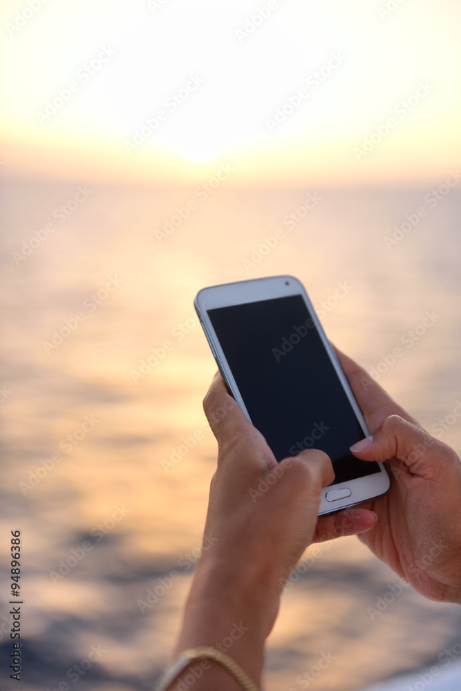 Smart phone close up - woman using smartphone app at ocean sunset at sea by the beach.