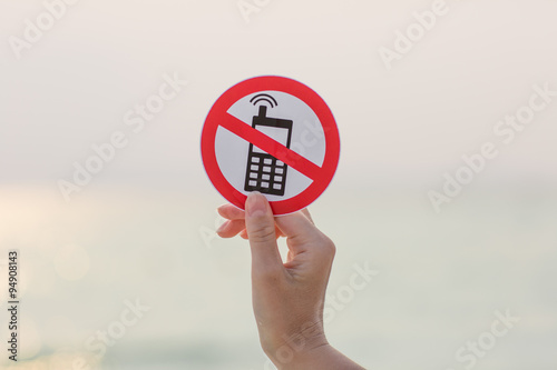 Female hand holding "No phone calls" sign on the beach on sea background
