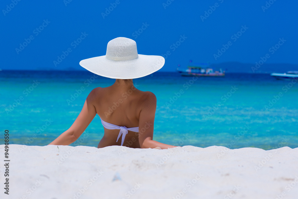 Woman in white hat lying on the beach, blue sea and sky background