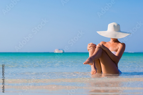 Woman in white hat sitting on the beach, blue sea background