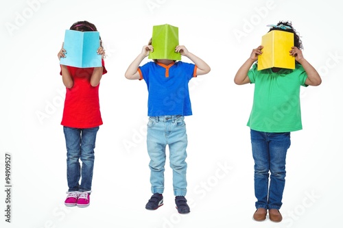 Three kids standing with books in front of their faces