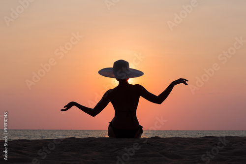 Woman silhouette with hat sitting on sunset sea background  back lit