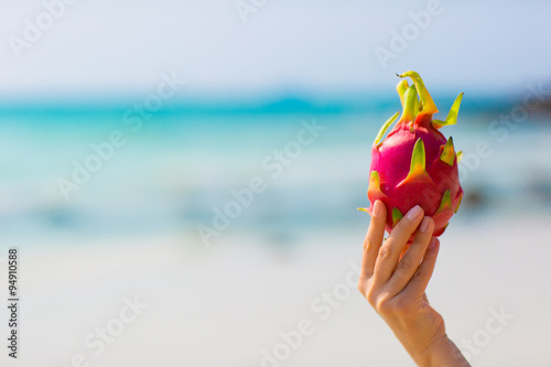 Female hand holding a dragon fruit on blue sea background