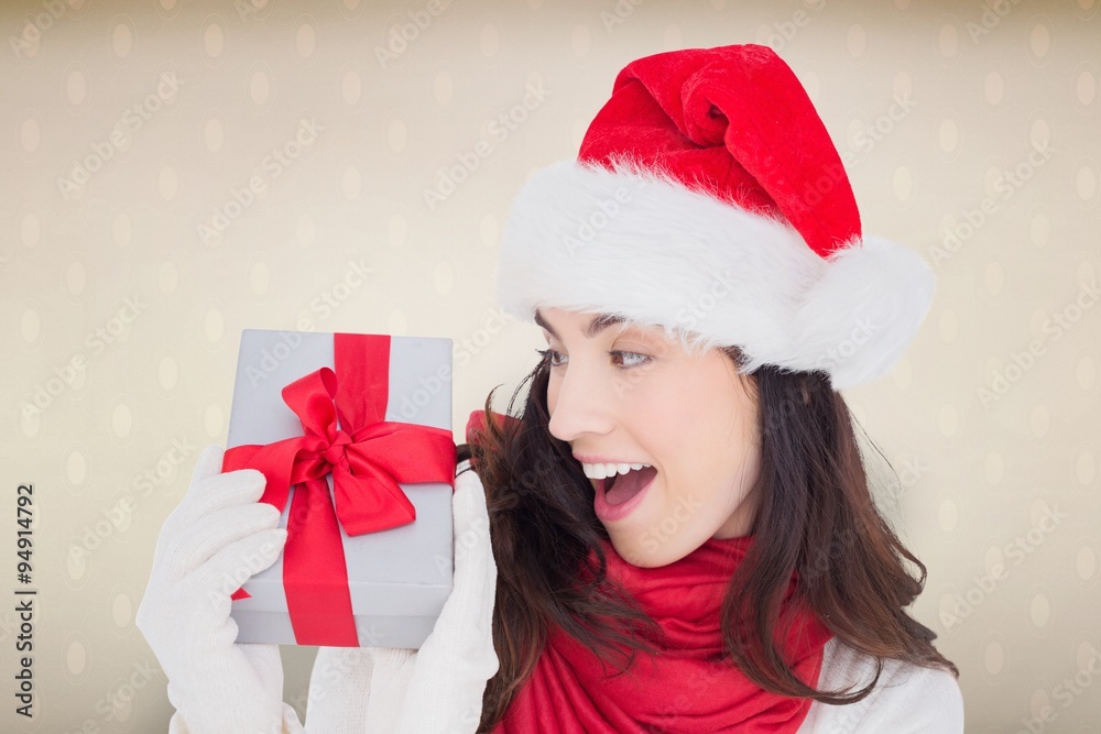 Composite image of astonished brunette in santa hat showing gift Composite image of astonished brunette in santa hat showing gift