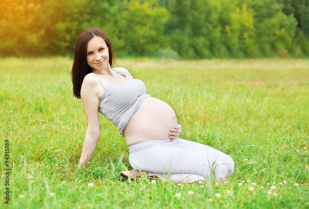 Happy smiling pregnant woman resting on grass in summer day Happy smiling pregnant woman resting on grass in summer day