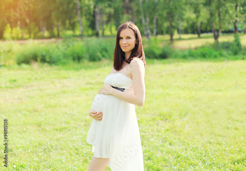 Beautiful young pregnant woman in white dress on nature