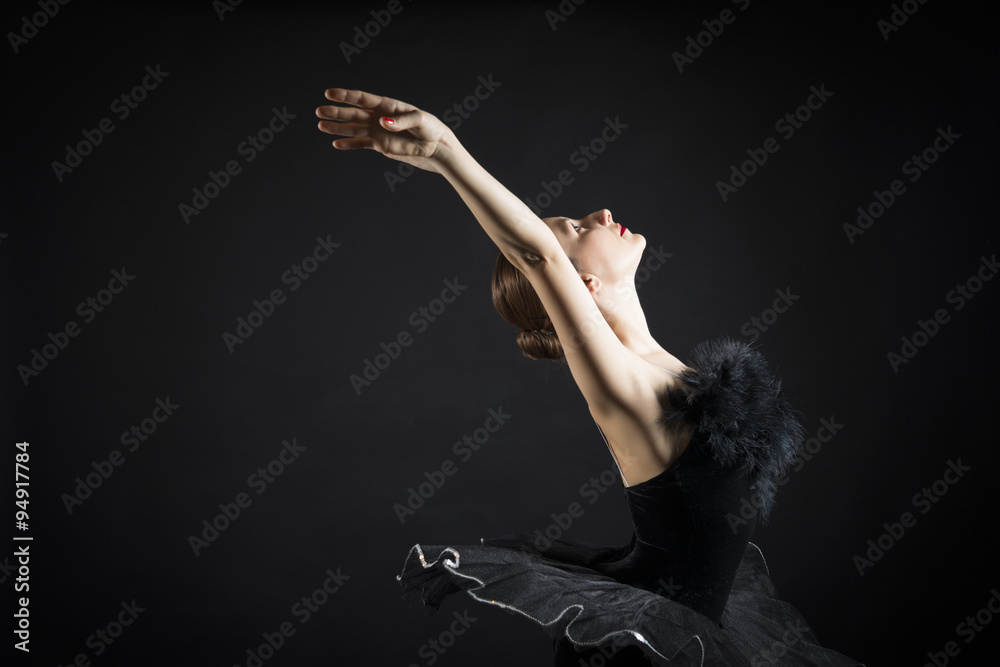 Fototapeta premium Beautiful expressive ballerina in the role of a black swan, wearing black tutu and pointe shoes on black background